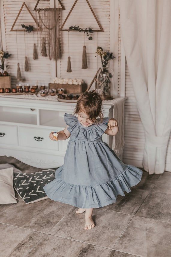 Boho-style toddler girl in a flowy blue ruffle dress playing indoors