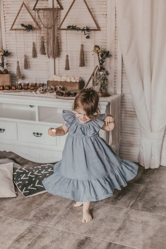 Boho-style toddler girl in a flowy blue ruffle dress playing indoors