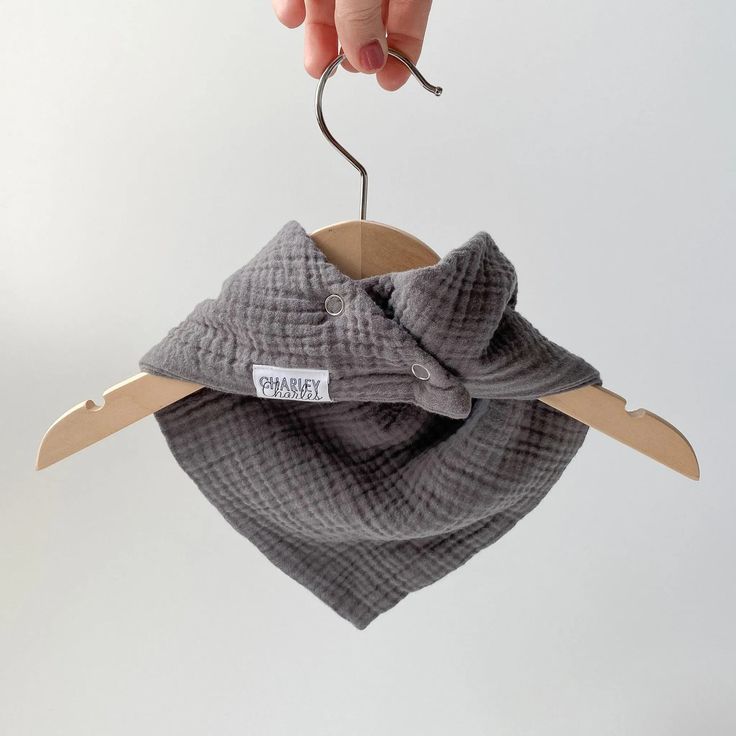 Gray muslin bandana bib hanging on wooden hanger

