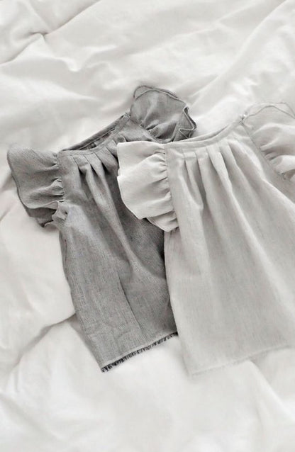 Two baby girl puff sleeve tops, one dark grey and one light grey, folded on a white textured surface.