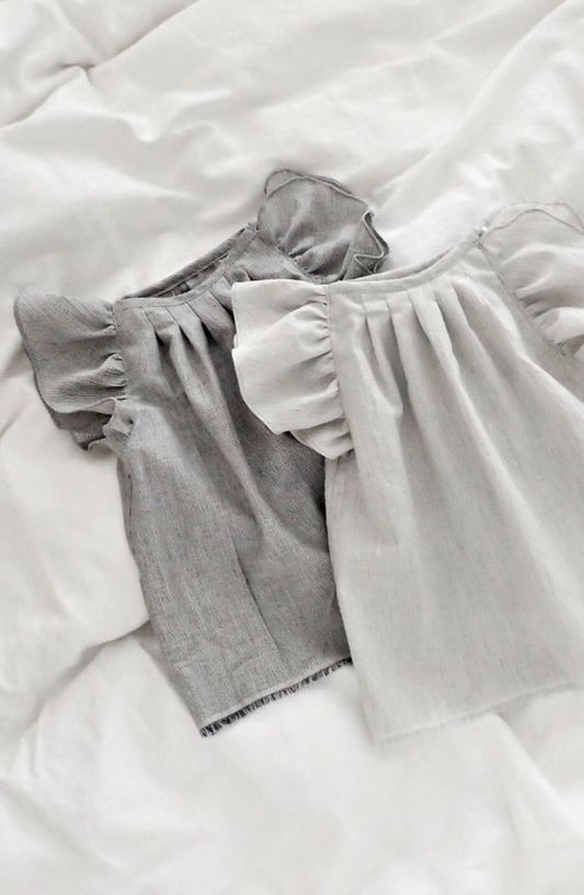 Two baby girl puff sleeve tops, one dark grey and one light grey, folded on a white textured surface.