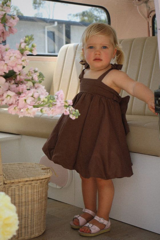 Girl posing in stylish brown baby dress with pink sandals
